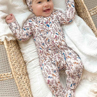 Baby in a floral onesie and headband lying in a woven basket with white blanket
