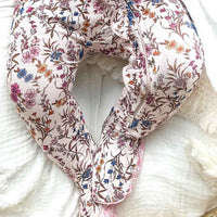 Floral-patterned baby seat cover on a white blanket with a woven basket at the bottom.