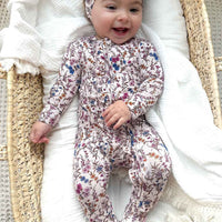 Baby in a floral onesie lying in a moses basket with white bedding
