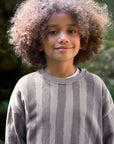 Child wearing a gray sweater with a blurred green background