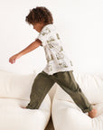 Child in a white shirt with a map design and green pants standing on a white couch.