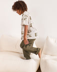 Child wearing a patterned shirt and green pants standing on a white couch.
