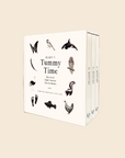 A boxed set of three art books titled "Baby's Tummy Time" by Tarantina Page, shown as a clean studio product shot on a warm off-white background. The box front features black-and-white animal illustrations including a butterfly, bird, dolphin, owl, skunk, fish, and chicken, with the title in large serif text.