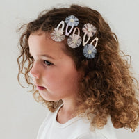 Young girl with curly hair wearing decorative hair clips against a plain background