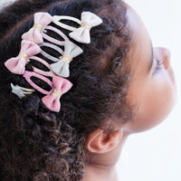 Child with curly hair wearing multiple decorative hair clips on a white background