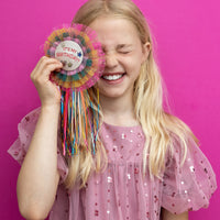 Young girl in a pink dress holding a colorful birthday badge against a pink background