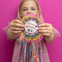 Young girl holding a colorful birthday decoration against a pink background