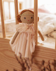 Small doll with a pink dress hanging inside a wooden crib