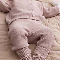 Baby in a pink knitted outfit lying on a beige blanket