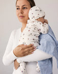 Woman holding a baby wrapped in a swaddle blanket against a plain background