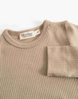 A close-up of a ribbed knit crewneck sweater in a light taupe-beige color, with a folded cuff showing the ribbed texture and a visible MarMar Copenhagen brand label.