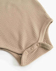 Close-up of a beige ribbed knit baby bodysuit showing the shoulder and snap-button crotch area on a white background.
