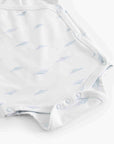 A close-up of a white baby bodysuit featuring a delicate light blue leaf pattern and snap closures along the shoulder and crotch.