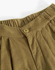 Close-up of olive brown corduroy pants showing the elastic waistband, button closure, and pleated fabric texture.