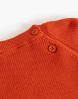 Close-up of a textured knit orange sweater with two brown buttons at the collar, set against a plain white background.