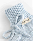 A close-up of a light blue knit baby bootie with a matching knotted tie and a beige fabric tag reading 'Mamam'.