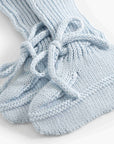A close-up of a pair of light blue hand-knit socks with a lace-up design, shown on a clean white background.