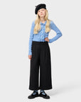 Person wearing a blue cardigan, black beret, and black wide-leg pants on a white background