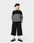 Person wearing a black and white striped sweater, black beret, and black pants on a white background