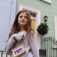 Young girl standing in front of a green house with a small bag
