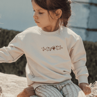 Child wearing a beige sweatshirt with a floral design outdoors