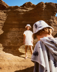 Two children in hats standing in a desert landscape with rocky formations.