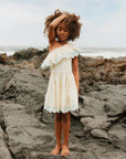 Young girl in a white dress standing on rocky terrain with a coastal background