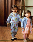 Two children in matching outfits standing on a wooden floor with wooden crates in the background.