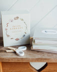 Stack of books titled 'Our Little Library' on a wooden surface with a white background