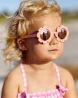Young girl wearing pink sunglasses and a pink dress on a beach.
