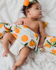 Baby wrapped in a cloth with orange pattern on a white blanket