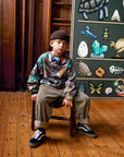 Child sitting on a chair in front of a chalkboard with educational drawings.