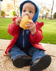 Child in a red and blue jacket eating a sandwich outdoors