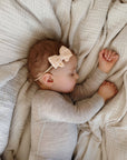 Baby lying on a soft blanket wearing a beige bow headband.