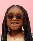 Young girl with braided hair wearing sunglasses against a pink background