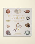 Our Big Book of Sports children's book with a white cover featuring watercolor illustrations of various sports items, photographed on a light cream background.