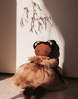 Textile doll with dark hair and a beige dress in soft lighting