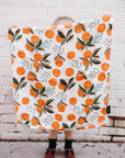 Person holding a blanket with orange pattern against a white brick wall.