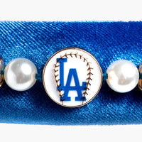 Blue bracelet with pearls and a baseball team logo charm on a white background