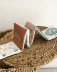 Four small books with animal illustrations on a woven mat.