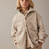 Person wearing a beige coat and cargo pants against a plain background