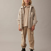 Child wearing a beige jacket and pants on a plain background
