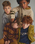 Four children posing together in cozy, vintage-style knit and cotton clothing against a solid gray studio background.