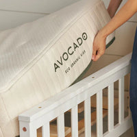 Person placing an Avocado eco organic crib mattress on a white crib.