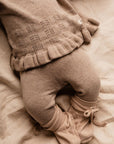 Sepia-toned image of a child's legs wearing a patterned sweater and pants on a soft surface.