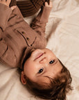 Baby wearing a brown sweater lying on a soft surface