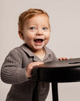 Child in a gray sweater holding a black object against a plain background