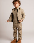 Child wearing a beige coat, sweater, pants, and boots on a plain background
