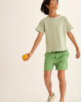 Child wearing a striped shirt and green shorts holding an orange against a plain background