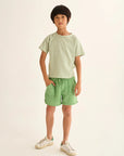 Child wearing a striped shirt and green shorts on a plain background